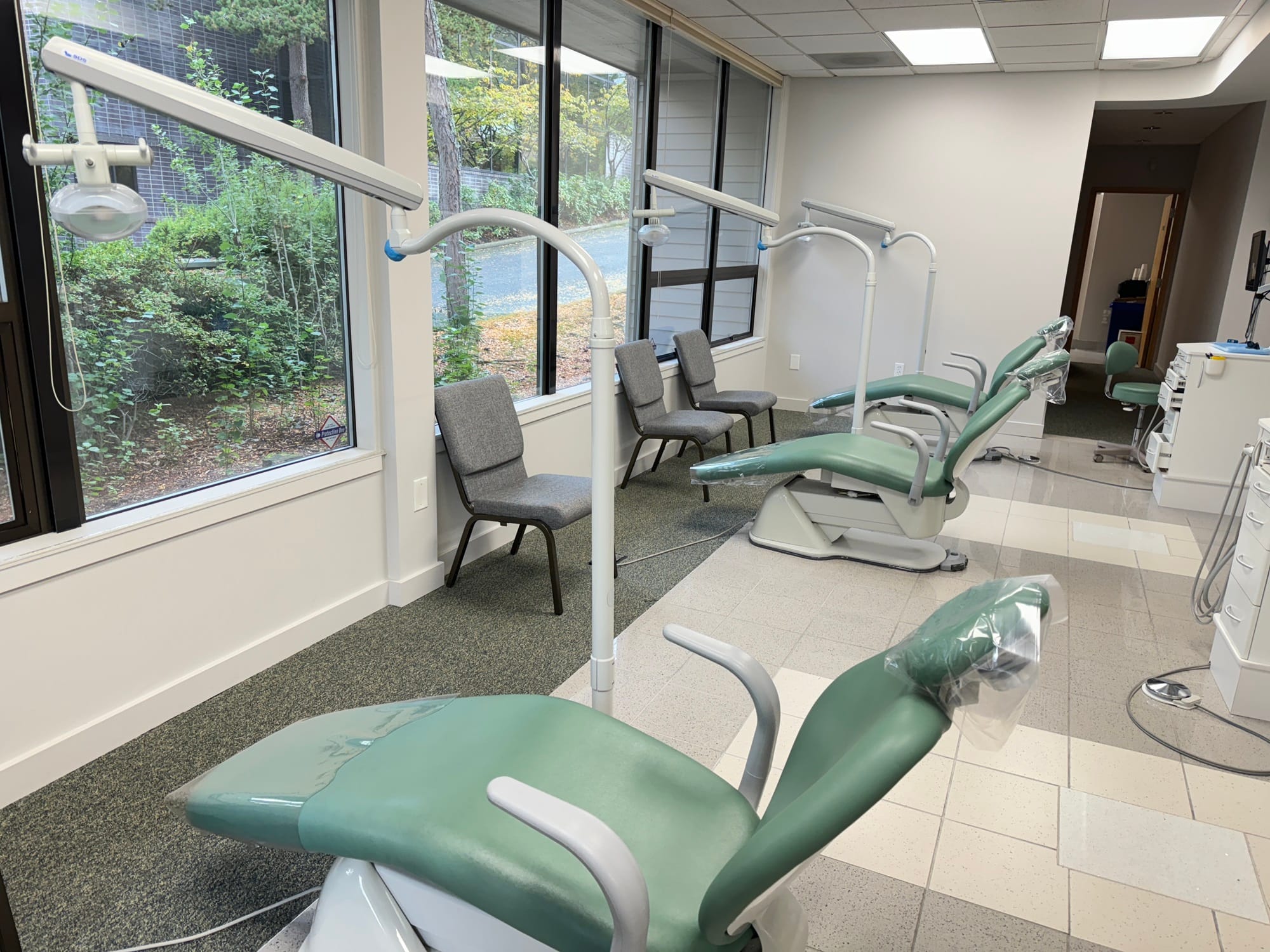 A dental clinic room with green dental chairs lined up next to large windows, offering views of greenery outside - Washington Orthodontics