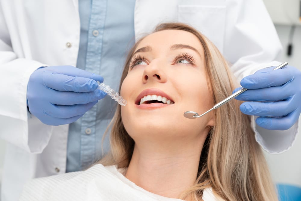 A smiling woman holding a tablet stands in an office environment, with colleagues working in the background - Washington Orthodontics