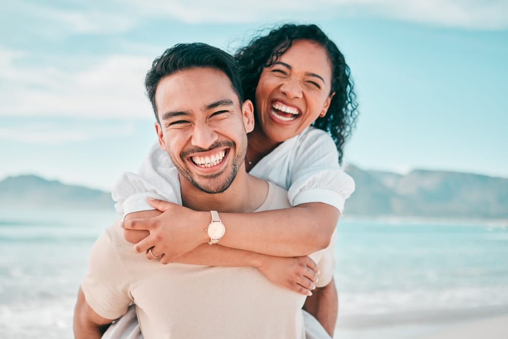 A young couple with beautiful teeth smiling by the water